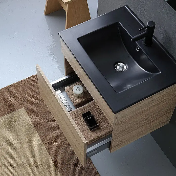 Kiamami Valentina Badmöbel-Set - Helles Holz - Helles Badezimmermöbel aus Holz mit schwarzem integriertem Waschbecken und teilweise geöffneter Schublade mit Toilettenartikeln.
