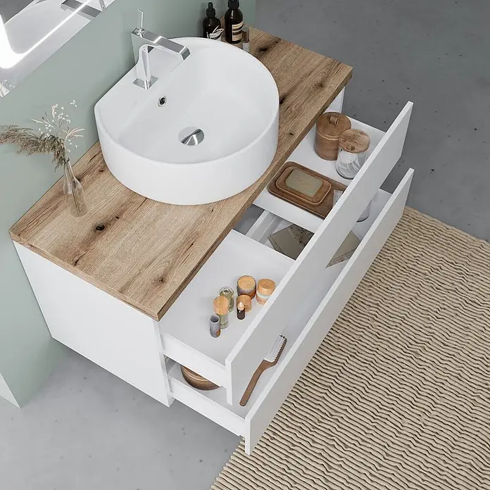 Kiamami Valentina Badmöbel-Set - Weiß - Weißer Badunterschrank mit heller Holzplatte und weißem Waschbecken, zwei offene Schubladen mit Toilettenartikeln.