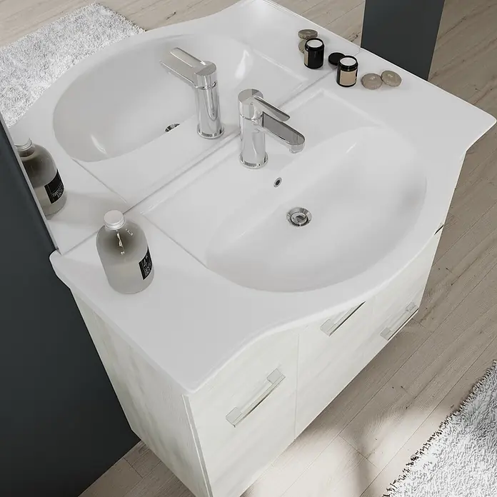 Kiamami Valentina Badmöbel-Set - Weiß - Weißer Doppelwaschtisch mit hellem Holzschrank, Chromarmaturen und Toilettenartikeln in einem modernen Badezimmer.