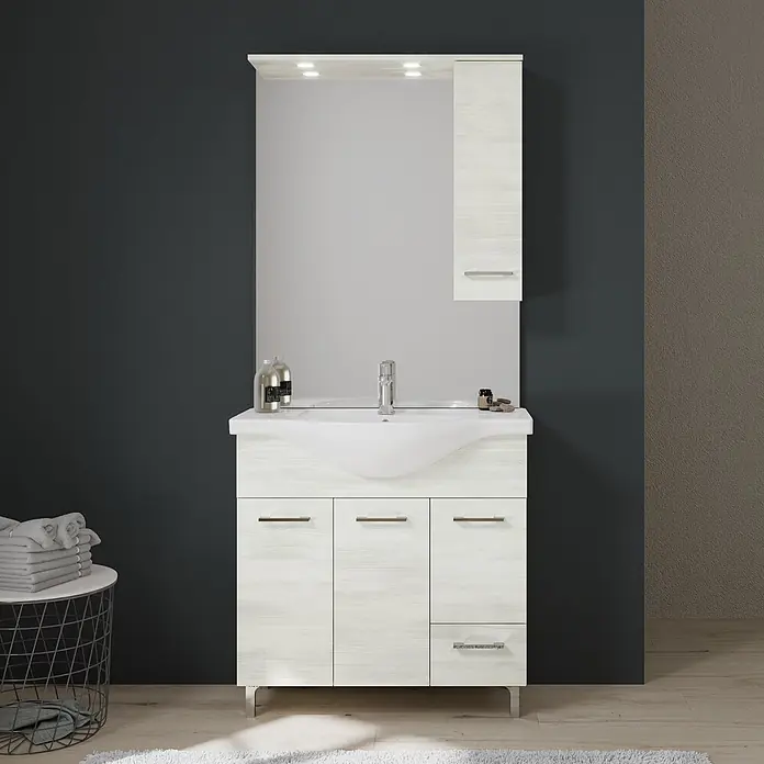 Kiamami Valentina Badmöbel-Set - Weiß - Badezimmermöbel aus hellem Holz mit weißem Waschbecken, Spiegel und Lagerschrank, in modernem Badezimmer.