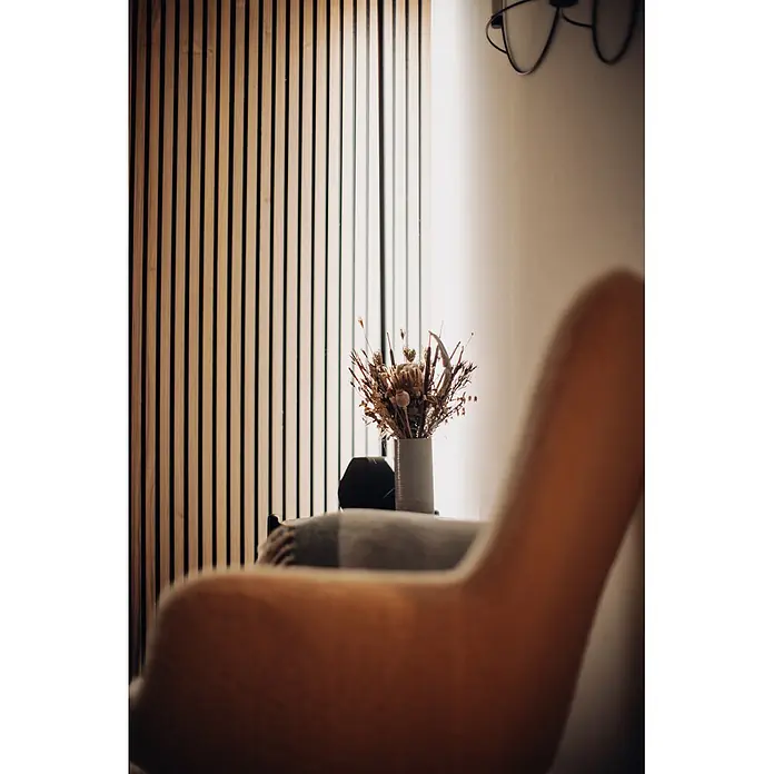 Ledvance Smart+ WiFi LED-Wandleuchte Floor Corner - L x B x H: 142 x 11 x 72 cm, Aluminum, Kaltweiß - Eine graue Vase mit einem Trockenblumenarrangement, einschließlich Samenkapseln und Schilf, auf einem Beistelltisch vor einer Holzlamellenwand.