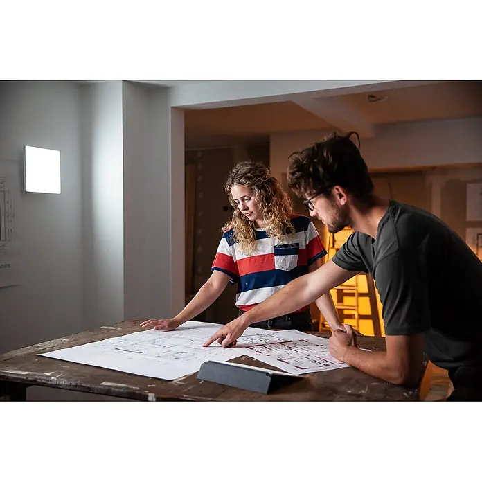 Ledvance Smart+ LED-Wand- & Deckenleuchte Planon Frameless - 20 W, L x B x H: 30 x 30 x 6,2 cm, Neutralweiß - Zwei Personen prüfen Baupläne auf einem Holztisch, einer zeigt auf Details. Ein Tablet liegt daneben, deutet auf Designarbeit hin.