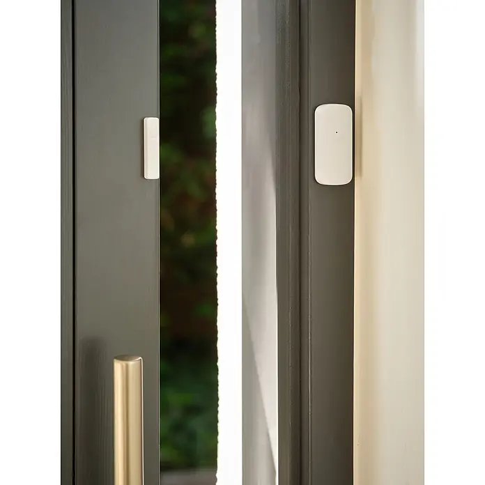 Ledvance Smart+ WiFi Funk-Fensterkontakt - Weiß, 3,1 x 2,4 x 7,2 cm - Zwei Teile eines weißen Smart-Home-Kontaktsensors an einer offenen dunkelgrauen Tür und dem Rahmen.