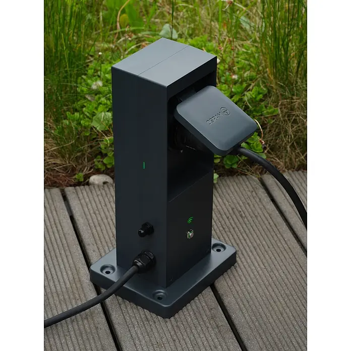 Ledvance Smart+ WiFi Energiesäule mit integriertem WLAN-Repeater und zwei smarten Steckdosen - Anthrazit - Dunkelgraue elektrische Ladestation mit angeschlossenem Kabel auf Holzterrasse im Freien. Mit grünen Anzeigen und OSRAM-Stecker.