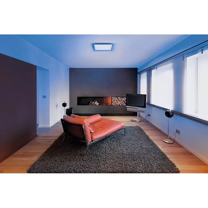 Osram Smart+ LED-Panel Planon Plus - L x B x H: 45 x 45 x 5,6 cm, Weiß, RGBW - Modernes Wohnzimmer mit hellem orangefarbenem Sofa, dunkelgrauem Hochflorteppich, integriertem Kamin und TV, beleuchtet von kühlem blauem Licht.