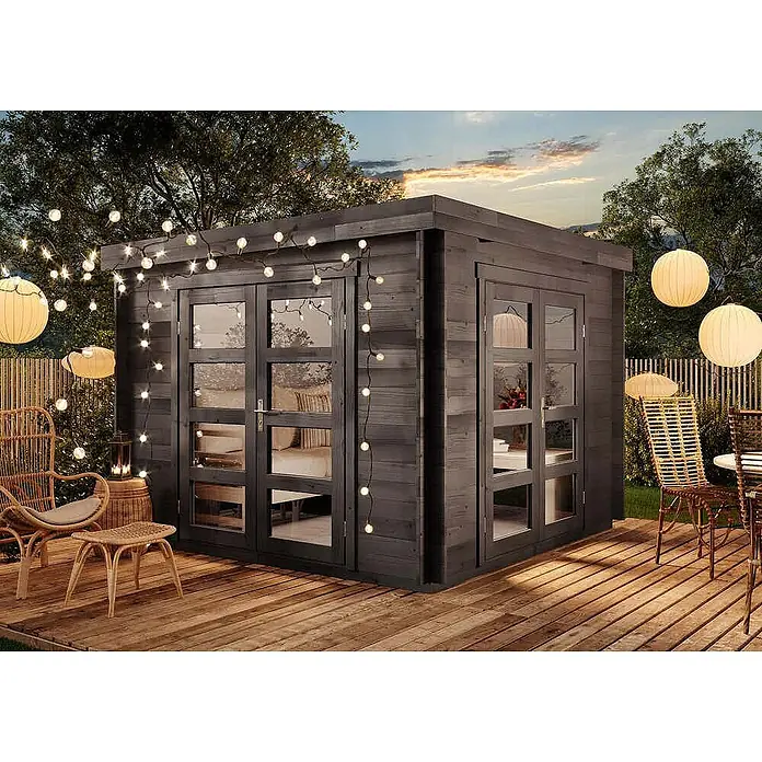 Alpholz Gartenhaus Paloma Beach - Außenmaß inkl. Dachüberstand (B x T): 298 x 298 cm, Holz, Anthrazitgrau - Moderner Gartenschuppen aus dunklem Holz mit großen Glastüren auf einer Holzterrasse, dekoriert mit Lichterketten für einen abendlichen Wohnraum im Freien.