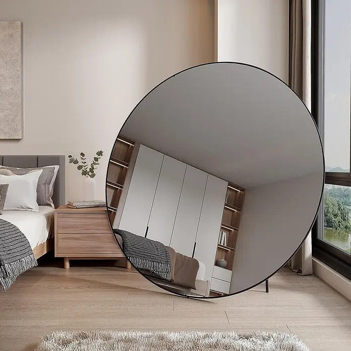 Home Deluxe Standspiegel KALI -  - Großer runder Spiegel mit schwarzem Rahmen lehnt in einem Schlafzimmer und reflektiert Kleiderschrank und Bett.