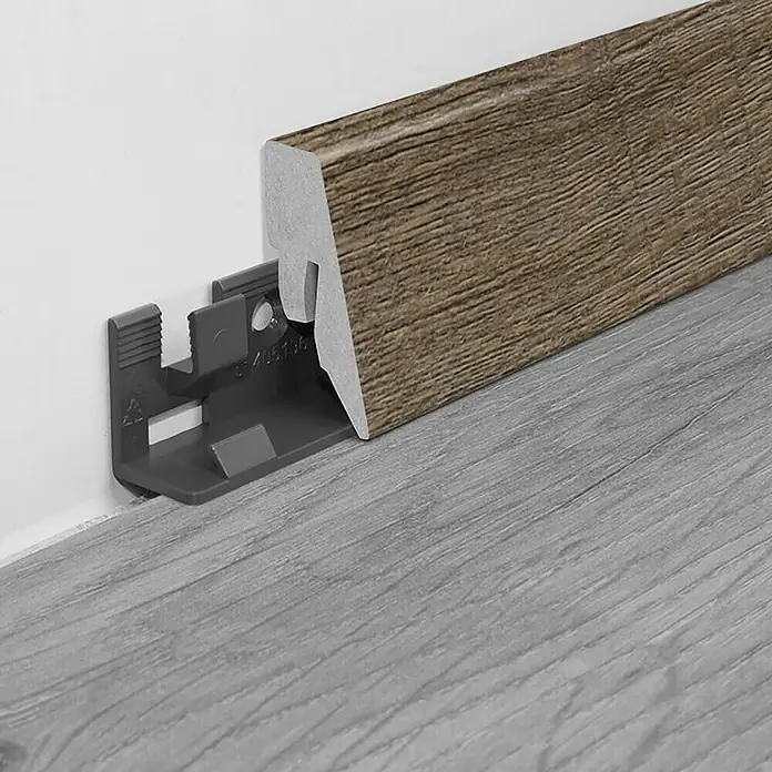 LOGOCLIC Sockelleiste K40 C Driftwood - 260 cm x 19 mm x 40 mm, MDF - Nahaufnahme einer braunen Sockelleiste mit Befestigungsclip. Detailaufnahme von Boden und Wand für Renovierung.