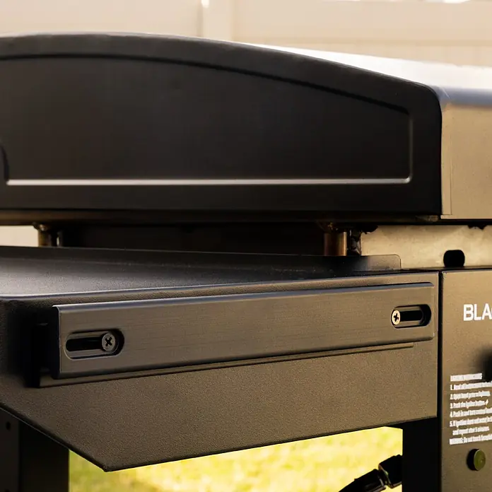 Blackstone Plancha-Grill 28" Omnivore - Grillfläche (B x T): 73 x 45,7 cm, 10 kW, Anzahl Brenner: 2 Stk. - Detailaufnahme der strukturierten Metallseite eines schwarzen Outdoor-Grills, mit Querstrebe, Justierschraube und teilweisem Branding.