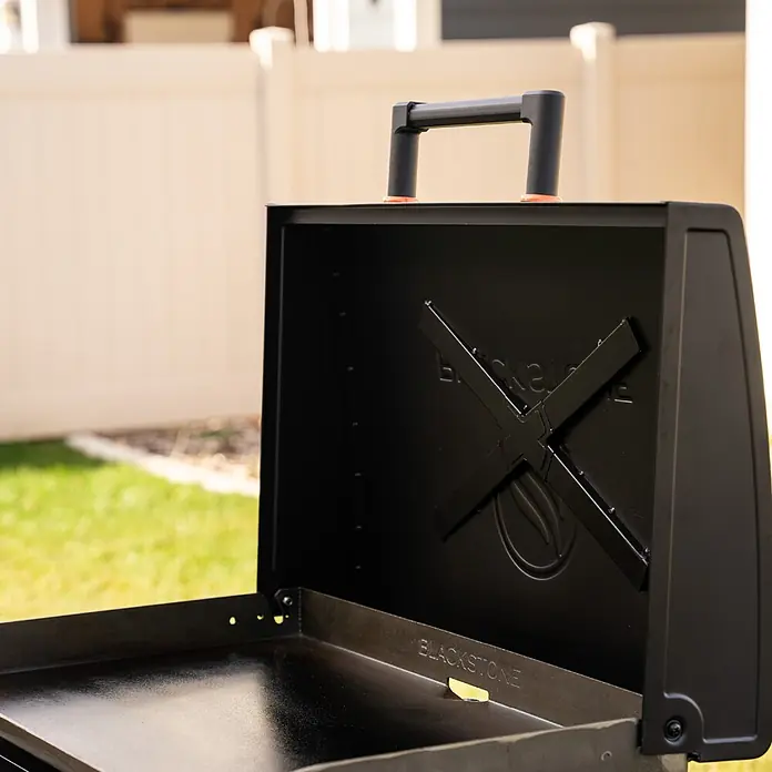 Blackstone Plancha-Grill 28" Omnivore - Grillfläche (B x T): 73 x 45,7 cm, 10 kW, Anzahl Brenner: 2 Stk. - Offener schwarzer Blackstone Grill mit hochgeklapptem Deckel, der die Kochfläche und das geprägte Logo im Deckel zeigt. Bereit zum Grillen.