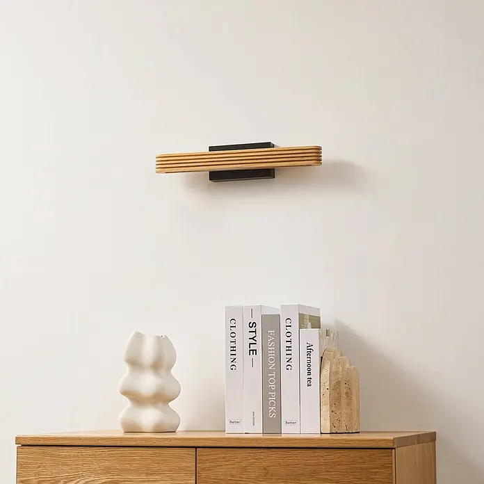 Lucande Wandleuchte Lieske - Holz hell - Wandleuchte mit horizontalem Holzlamellenschirm und schwarzem Rechtecksockel, die nach unten strahlt. Über einer Holzkommode angebracht.