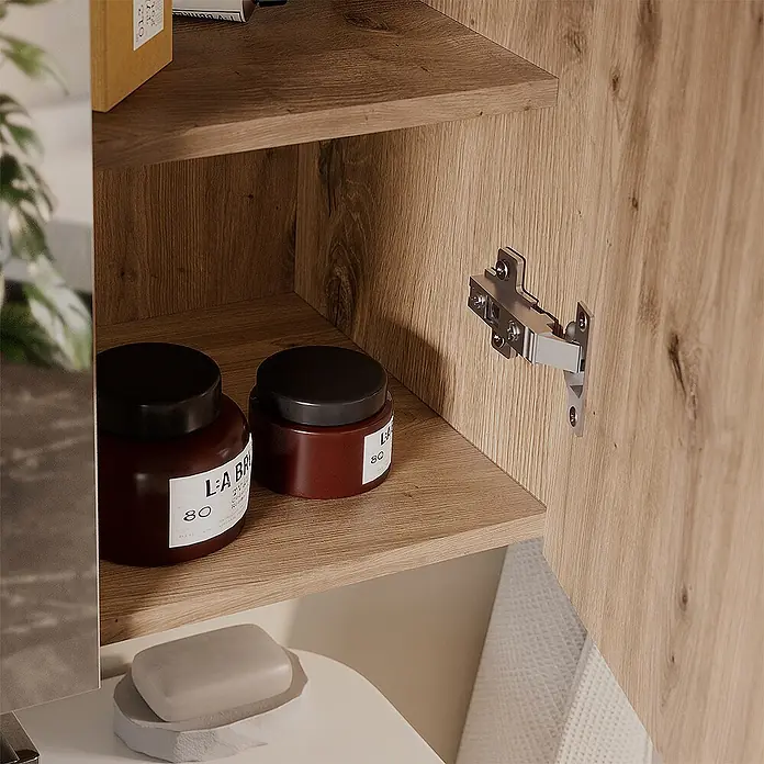 Vicco Badmöbel-Set Takumi Artisan 4 Teile - Gesamtbreite Badmöbel: 120 cm, Artisan-Eiche, Matt - Offener heller Holzschrank mit zwei Regalböden, darauf zwei dunkelbraune Tiegel und eine graue Seife auf einem weißen Tablett darunter. Ein silbernes Scharnier ist sichtbar.