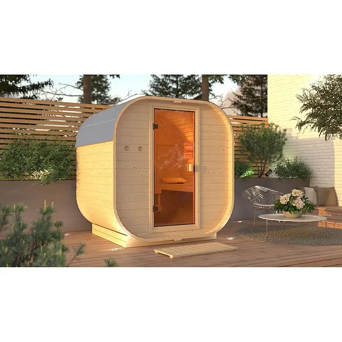 Karibu Saunahaus Skadi 1 - 9 KW Ofen mit interner Steuerung, Natur, L x B x H: 175 x 199 x 205 cm - Ovalförmige Außensauna aus hellem Holz mit Glastür und warmem Innenlicht, auf Holzdeck im Garten.