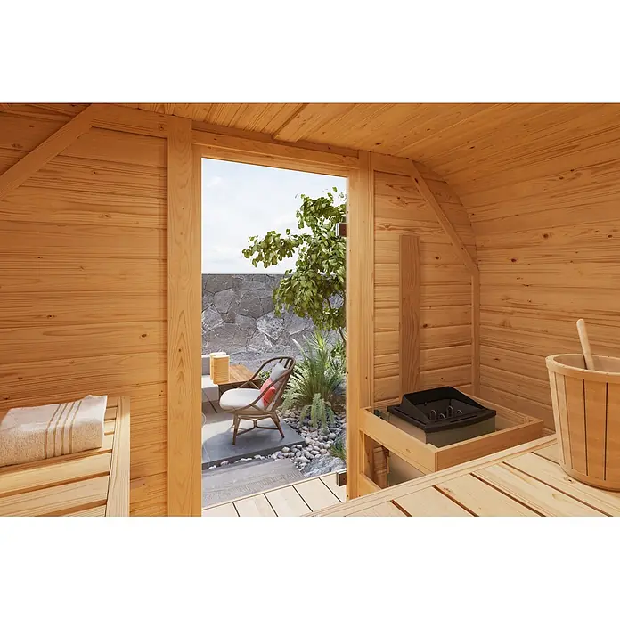 Karibu Saunahaus Quadro 1 Plus - 9 KW Bio-Ofen mit externer Steuerung, Natur, L x B x H: 385 x 225 x 205 cm - Holzt sauna-Interieur mit Lattenwänden und Bänken, Heizung und Holzeimer mit Schöpfkelle. Blick auf eine Außenterrasse mit Sitzgelegenheiten.