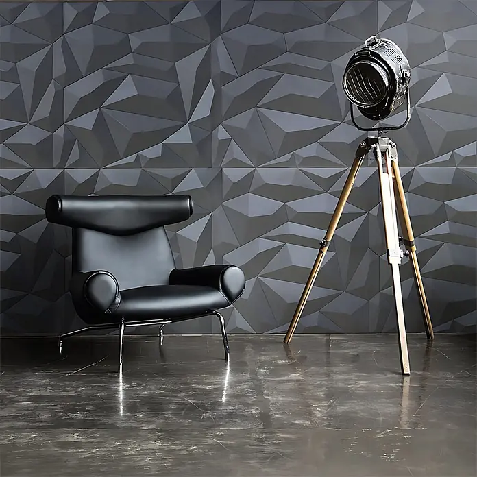 Profhome Wandpaneel 3D 705390 Glacier Smoked Gray Dekorpaneel abstraktes Muster grau 2 m2 - 610 x 600 mm - Schwarzer Ledersessel und Vintage-Scheinwerfer auf Holzstativ vor dunkelgrauer 3D-Geometrie-Wand auf glänzendem Boden.