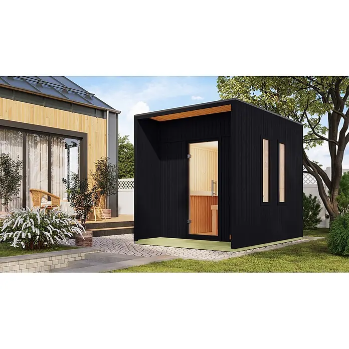 Karibu Saunahaus Laguna - L x B x H: 287,5 x 219,5 x 244 cm, Schwarz, Ohne Ofen - Moderne schwarze Außensauna mit Holzinterieur, Glastür und zwei schmalen Fenstern, im Garten neben einem modernen Haus.