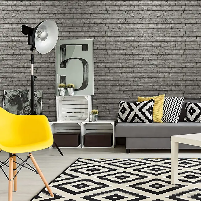 Profhome Wandpaneel 3D 704500 Ledge Stone Portland Cement Dekorpaneel Stein Optik grau 2 m2 - 610 x 600 mm - Graue Tapete mit Ziegelmuster bedeckt eine Wohnzimmerwand und bietet eine moderne, strukturierte Kulisse.