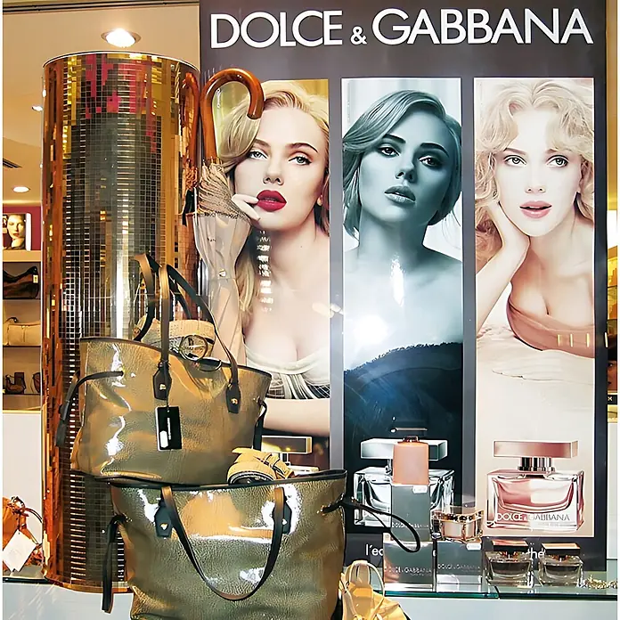 Wallface Wandpaneel 27375 M-Style Design Platte Wand-paneel Deko selbstklebend gold 0,96 qm - 980 x 980 mm - Dolce & Gabbana Verkaufsdisplay mit glänzenden grünen Tragetaschen, Luxusparfüms und Prominentenwerbung.