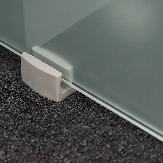 Inova Schiebetür-Komplettset Glas Komplettset wellenförmig mit Griffmuschel + Softclose - 1.025 x 2.200 mm - Hellgraue Halterung, die eine klare Glasplatte auf dunklem, strukturiertem Untergrund hält.