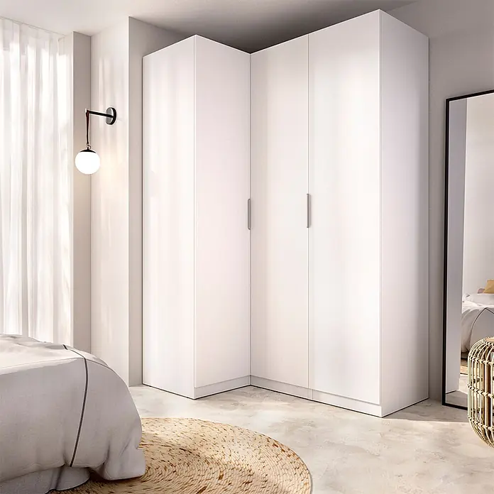 Dekit Armario para ropa Emax - L x An x Al: 95 x 142,2 x 203,5 cm, Blanco, Rinconero - Armario esquinero blanco en forma de L con acabado liso, instalado en un dormitorio moderno.