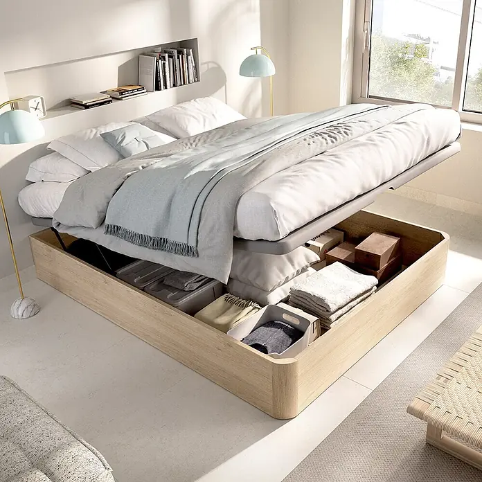 Dekit Canapé Round - 190 x 150 x 32 cm, Roble Cambrian, Abatible - Cama de madera clara con almacenaje bajo la cama abierto, mostrando ropa de cama y otros artículos. Ropa de cama blanca y gris claro.