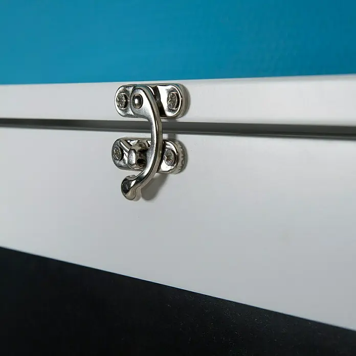 Phönix Wandschreibtisch York - L x B x H: 60 x 75,5 x 149 cm, Weiß/Schwarz - Nahaufnahme eines Kastenschlosses aus Metall an einer weißen Box mit blauem Hintergrund. Das detailreiche Design des Schlosses wird hervorgehoben.