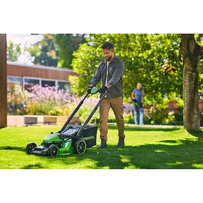 Greenworks Akku-Rasenmäher Gen2 GW 2X24V BL 46 cm - 48 V, 2 Akkus, 4 Ah, Schnittbreite: 33 mm - Ein Mann bedient einen grün-schwarzen Greenworks Rasenmäher und mäht Gras im Garten.
