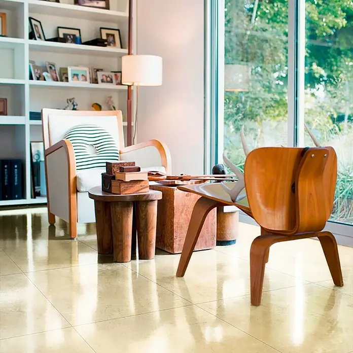 Feinsteinzeugfliese Premium Marble - 80 x 80 cm, Beige, Glänzend - Innenaufnahme eines Wohnzimmers mit einem Designerstuhl aus Holz, einem Sessel und einem Bücherregal, die ein stilvolles Ambiente schaffen.