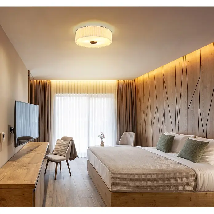 Globo Deckenleuchte rund Jannie - 40 W, Ø x H: 500 x 162 mm, E27 - Gemütliches Schlafzimmer mit Holzelementen, großem Bett, grünen Kissen und warmer Akzentbeleuchtung für entspannte Atmosphäre.