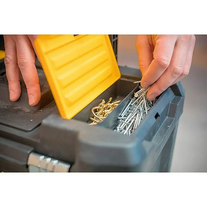 Stanley Rollende Profi-Box - Ohne Werkzeug, L x B x H: 47,5 x 28,5 x 62,3 cm - Nahaufnahme einer Person, die eine schwarze Werkzeugkiste mit gelbem Deckel öffnet und Nägel und Schrauben entnimmt.