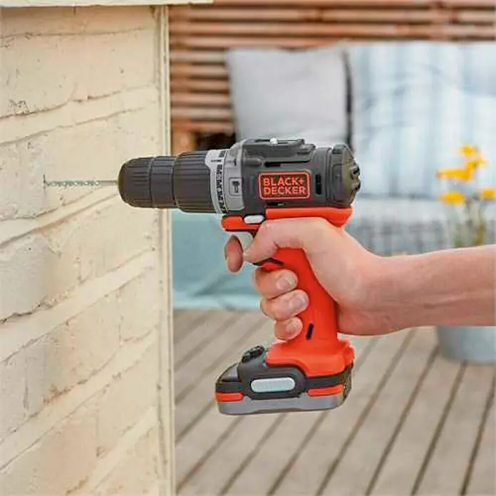 Black+Decker Taladro atornillador percutor de batería BDCHD12S1-XJ - 12 V, 1 batería, 40 Nm - Una persona está perforando un agujero en una pared con un taladro inalámbrico Black+Decker. La herramienta es naranja y negra.
