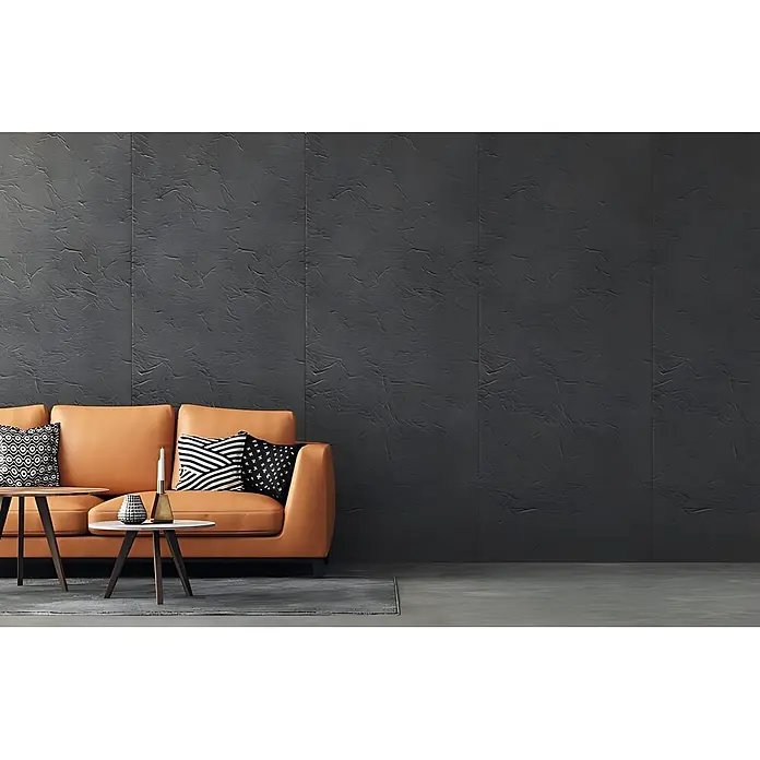 Wallface Wandpaneel 22717 CREPA VELVET Volcano Wandverkleidung in Leder Optik matt grau 2,60 m2 - 2.600 x 1.000 mm - Braunes Ledersofa mit gemusterten Kissen und Beistelltischen in einem modernen Wohnzimmer vor einer dunklen strukturierten Wand.
