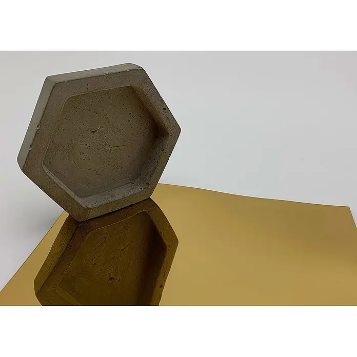 Wallface Wandpaneel 27823 OCEAN Gold Wandpaneel in Metall-Optik spiegelnd gold 2,6 m2 -  - Hexagonales graues Betontablett auf einer goldenen reflektierenden Oberfläche, seine Spiegelung zeigend.