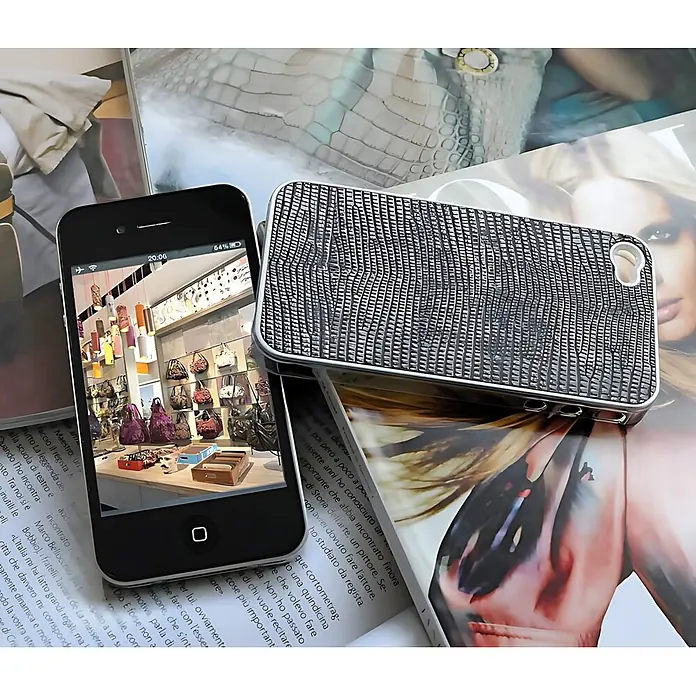 Wallface Wandpaneel 31669 LEGUAN Leder Wand-paneel selbstklebende schwarz 2,60 qm - silber - Silberne, strukturierte Handyhülle neben einem schwarzen Smartphone mit Ladeninterieur, beides auf Magazinen.