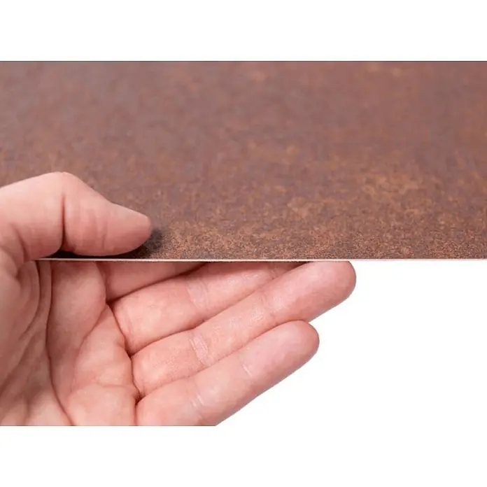 Wallface Wandpaneel 25548 Corten Nature Wandverkleidung im Used look matt braun 2,6 m2 - rot-braun, 2.600 x 1.000 mm - Eine Hand hält eine dünne, braune, texturierte Platte hoch, die ihre schmale Kante und gemusterte Oberfläche zeigt.