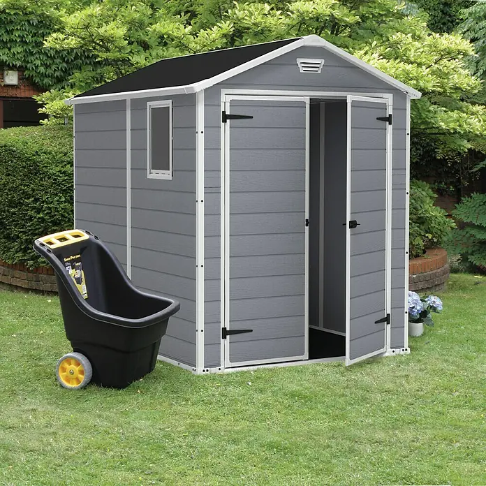 Keter Caseta de jardín Manor 6x8 - Medidas ext. (An x Pr): 185,8 x 236,8 cm, Gris Claro/Blanco, Plástico, Área: 3,9 m² - Un cobertizo de jardín gris con puertas abiertas, junto a una carretilla negra, muestra una solución de almacenamiento práctica para herramientas de jardinería.