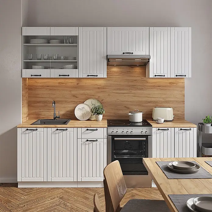 Vicco Küchenzeile Fame-Line Weiß Landhaus/Weiß ohne Arbeitsplatte - Weiß Landhaus, Ohne Elektrogeräte - Weiße Küchenschränke mit geriffelten Türen, schwarzen Griffen und heller Holztheke und -rückwand in einer modernen Küche.