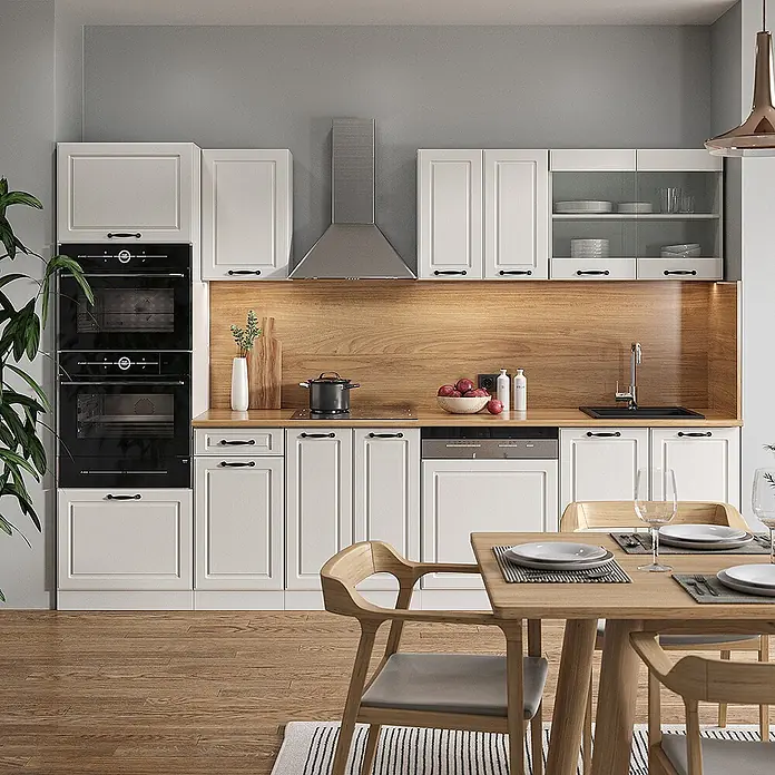 Vicco Küchenzeile R-Line Weiß Landhaus/Weiß mit Hochschrank, ohne Arbeitsplatte - Weiß Landhaus, Ohne Elektrogeräte - Eine moderne Küche mit cremefarbenen Schränken, Holzoptik-Rückwand und Arbeitsplatte, schwarzen Geräten und Esstisch im Vordergrund.