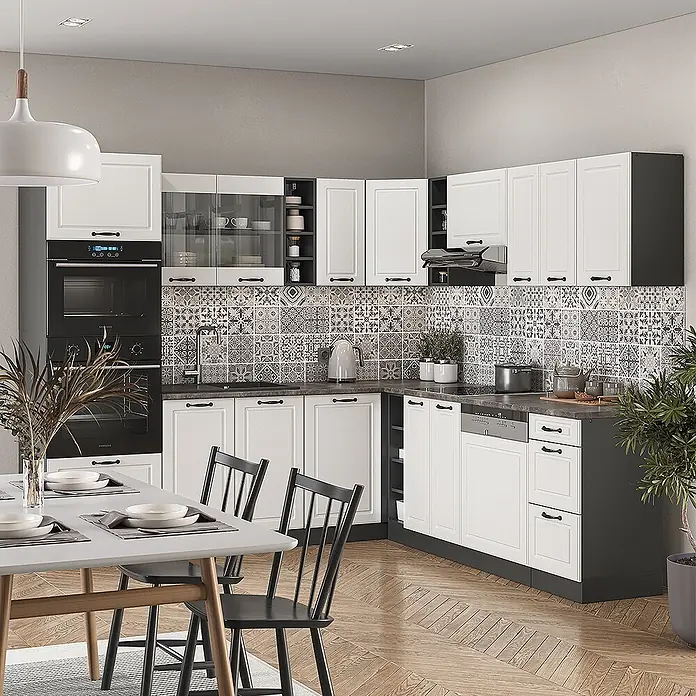 Vicco Eckküche R-Line Weiß Landhaus/Anthrazit, AP Eiche - B x T: 247 x 60 cm, Weiß Landhaus, Ohne Elektrogeräte - Moderne L-förmige Küche mit weißen Schränken, dunkelgrauen Arbeitsplatten, schwarzen Geräten und gemustertem Fliesenspiegel. Essbereich im Vordergrund.