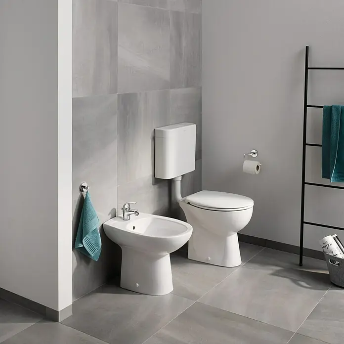 Grohe Essentials Bademantelhaken - Chrom, Glänzend - Das Bild zeigt eine moderne Toilette und ein Bidet in einem Badezimmer mit grauen Fliesen, minimalistischem Design und klaren Linien.