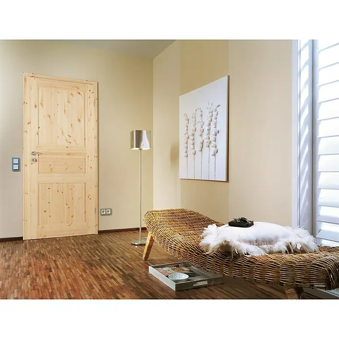 Kilsgaard Landhaustür 02/03 - 735 x 1.985 mm, DIN Anschlag: Rechts, Kiefer natur - Eine helle Holztür mit Paneelen fügt sich in ein Zimmer mit einem Korbstuhl, einer Stehlampe und Kunstwerk ein.