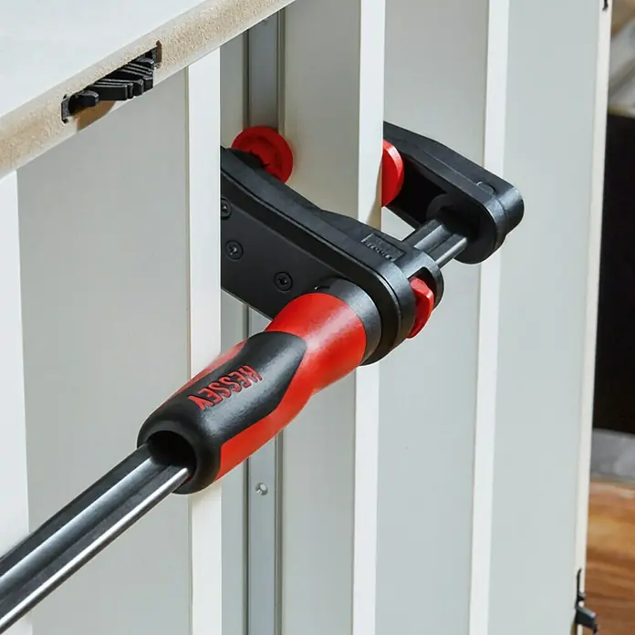 Bessey Getriebezwinge GearKlamp GK 30 - Spannweite: 300 mm, Spannkraft: 2.000 N, Ausladung: 60 mm - Nahaufnahme einer BESSEY-Stangenzwinge, die ein Werkstück fixiert und die robuste Bauweise sowie die Funktionalität des Werkzeugs hervorhebt.