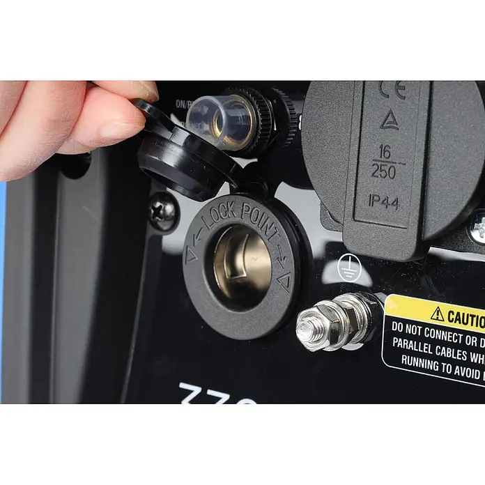 Ultimatron France Stromerzeuger ULT-3300 - Nennleistung: 3 kW, Tankvolumen: 4,2 l, Verbrauch: 2,3 l/h - Nahaufnahme einer Hand, die eine Schutzkappe auf einem schwarzen Bedienfeld mit Stromanschlüssen, Erdungsschraube und Warnaufkleber öffnet.