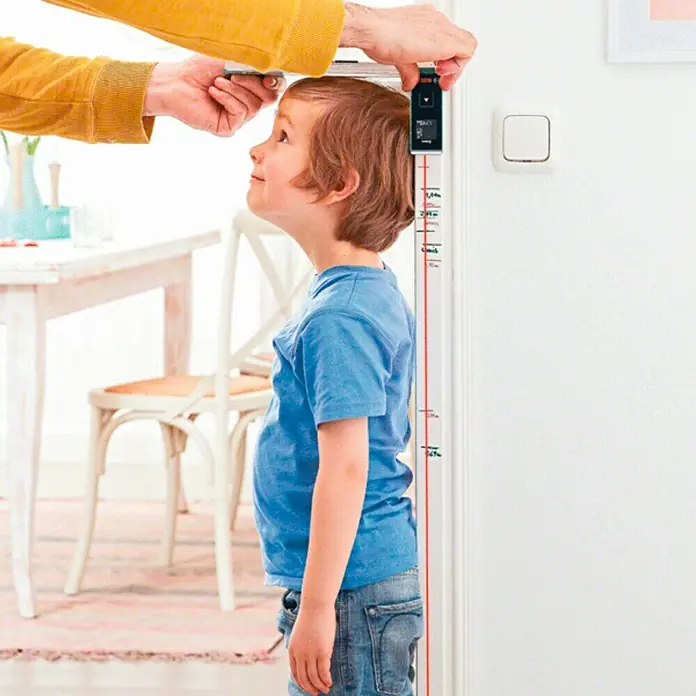 Bosch Medidor de distancia láser de bolsillo Zamo III - Gama de medición: 0,15 m - 20 m - Un niño está siendo medido con un dispositivo de medición digital fijado a una pared con marcas de altura.