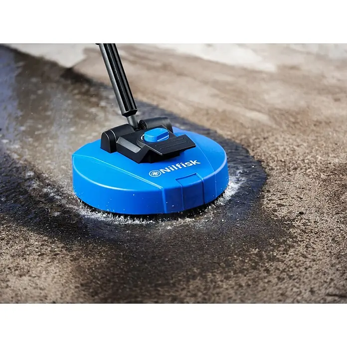 Nilfisk Hidrolimpiadora de alta presión CORE 150 PC - 150 bar, 2.000 W, Capacidad de bombeo: 468 l/h - Limpiador de patios Nilfisk azul limpiando activamente una superficie de hormigón sucia, rociando agua.