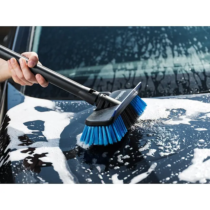 Nilfisk Hidrolimpiadora de alta presión CORE 140IH PCC - 140 bar, 1.800 W, Capacidad de bombeo: 474 l/h - Una persona usa un cepillo de lavado de coches negro y azul para limpiar un coche, creando espuma blanca.