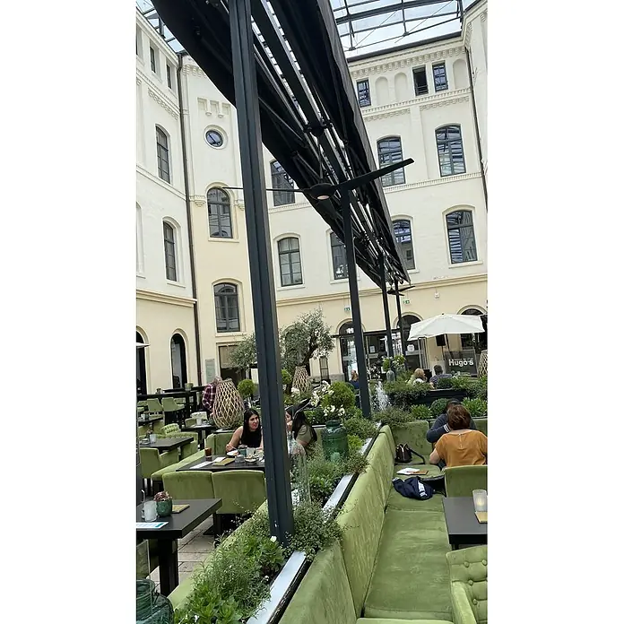 Vam Deckenventilator SPACE WI-FI schwarz 193 cm - schwarz, 1.930 mm, 45 W - Grüne Sitzgelegenheiten und Tische in einem belebten Restaurant-Innenhof mit Pflanzen und Gästen.