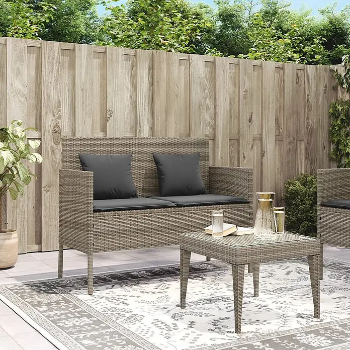 Furnicato Gartenbank PE-Rattan - B x T x H: 113 x 61 x 87 cm, Grau - Ein Outdoor-Sitzset aus hellbraunem Polyrattan, bestehend aus einem Zweisitzer-Sofa mit dunkelgrauen Kissen und einem passenden Couchtisch auf einer Terrasse.