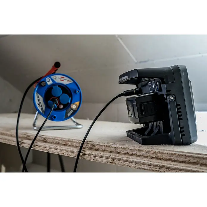 Brennenstuhl Mobiler LED-Strahler Multi Battery Hybridstrahler - L x B x H: 17,7 x 35,4 x 25,8 cm, IP55 - Blaue Kabeltrommel mit mehreren Steckdosen, verbunden mit einer schwarzen Arbeitsleuchte auf Holzfläche.