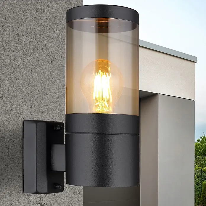 Globo Xeloo Außenwandleuchte - 60 W - Schwarze Außenwandleuchte mit bernsteinfarbenem Glaszylinder und sichtbarer Glühbirne an strukturierter Wand.